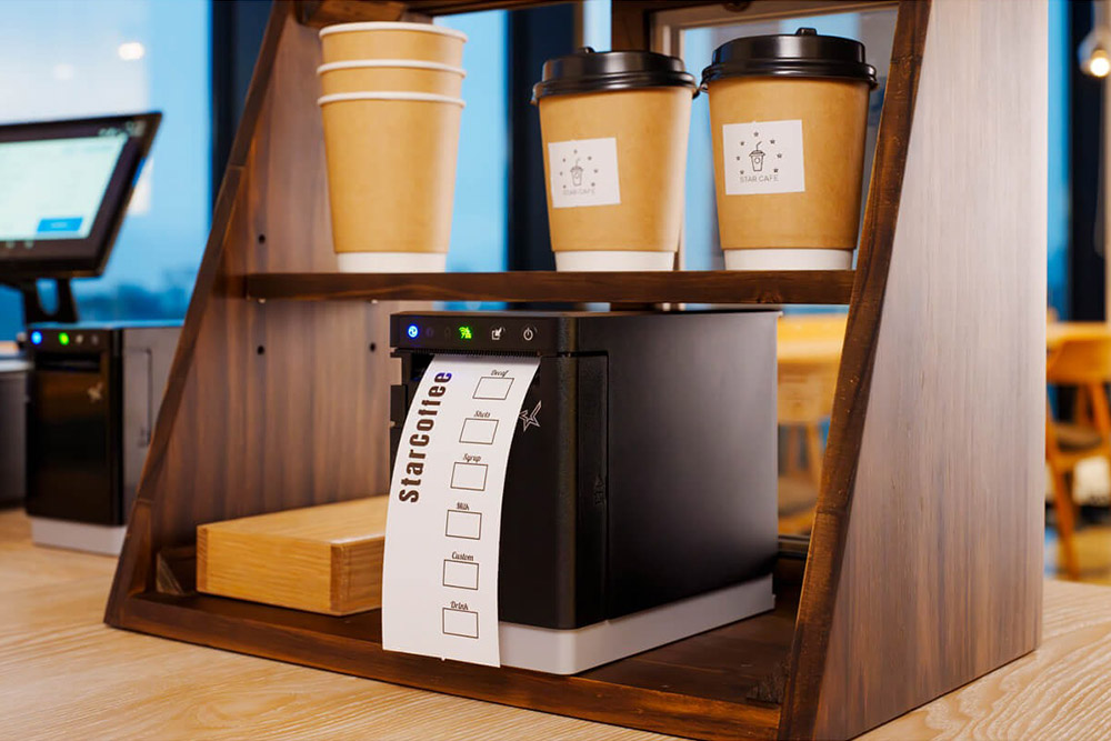 スター精密のサーマルラベルプリンターmC-Label2シリーズの本体をカウンター上の棚に収納したままラベルを印刷しているイメージ。前面排紙が採用されている。